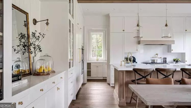 kitchen featuring wood finished floors, white cabinets, light countertops, a kitchen bar, and pendant lighting