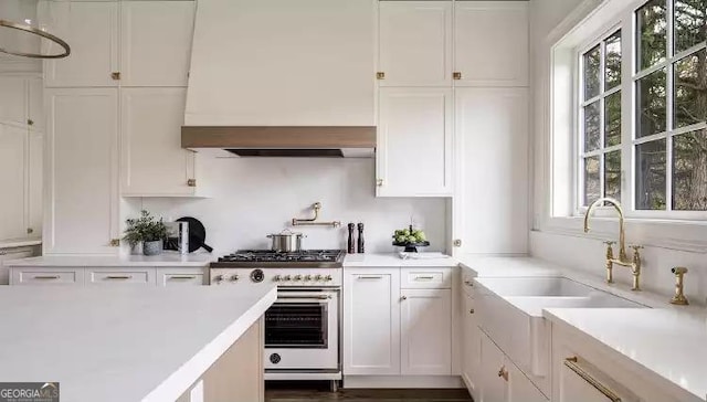 kitchen with a sink, white cabinets, light countertops, wall chimney range hood, and high end stainless steel range