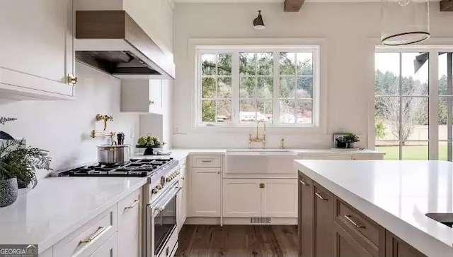 kitchen featuring dark wood-style flooring, gas range oven, light countertops, a sink, and wall chimney range hood