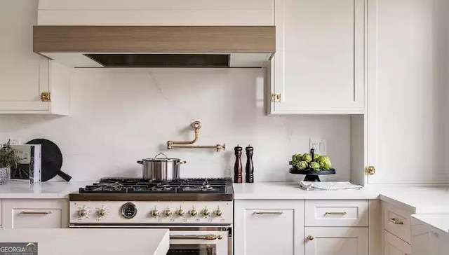 kitchen featuring light countertops, white cabinets, high end stainless steel range oven, and wall chimney range hood