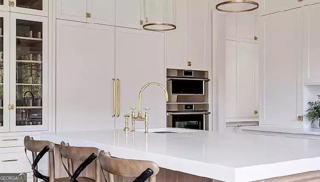 kitchen with white cabinets, glass insert cabinets, light countertops, stainless steel double oven, and a sink