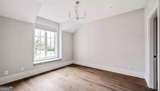 unfurnished dining area featuring a notable chandelier, baseboards, vaulted ceiling, and wood finished floors