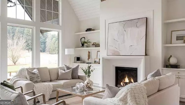 living room with high vaulted ceiling, built in shelves, and a glass covered fireplace