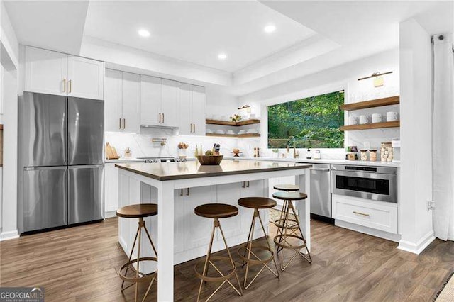 kitchen featuring dark wood finished floors, open shelves, a raised ceiling, appliances with stainless steel finishes, and white cabinetry