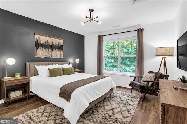 bedroom featuring baseboards, wood finished floors, visible vents, and a notable chandelier