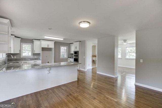 kitchen with a peninsula, a sink, white cabinets, stainless steel microwave, and dark wood finished floors