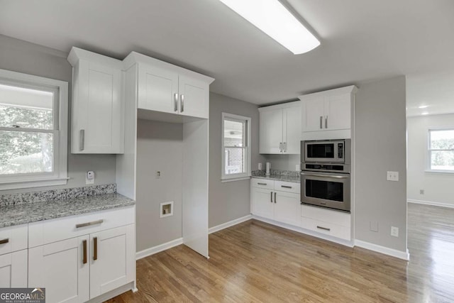 kitchen featuring appliances with stainless steel finishes, white cabinets, light wood finished floors, and light stone countertops