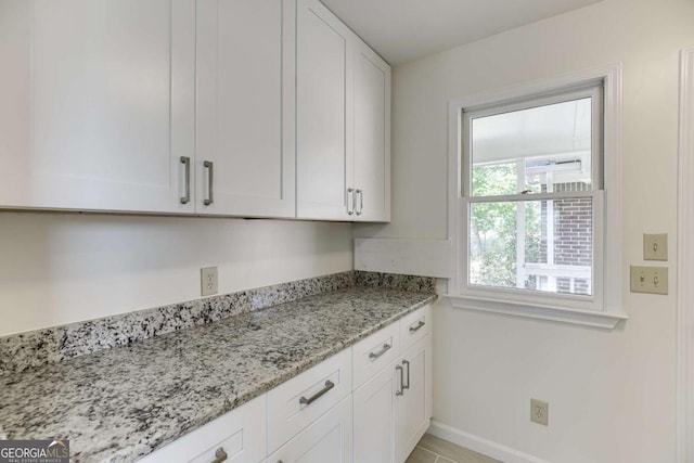 kitchen with light stone countertops, baseboards, and white cabinetry