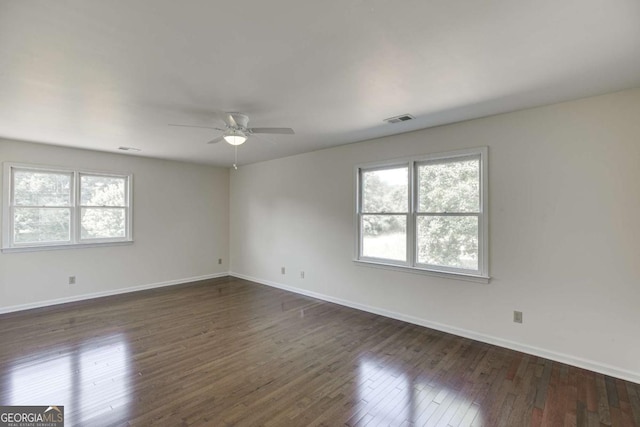 empty room with dark wood-style floors, visible vents, plenty of natural light, and baseboards