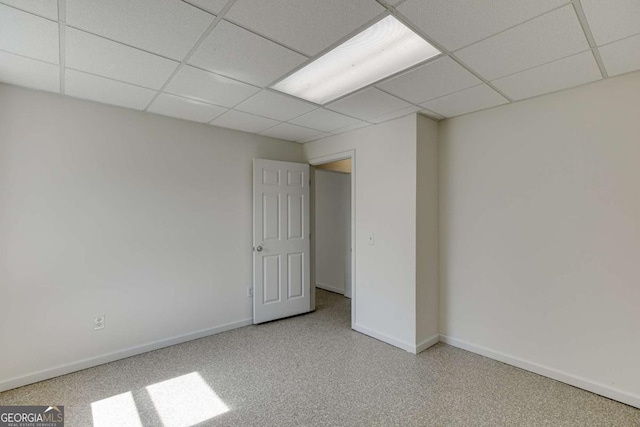 carpeted empty room featuring baseboards and a drop ceiling