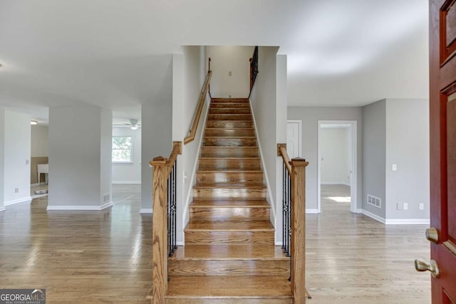 staircase featuring a ceiling fan, wood finished floors, visible vents, and baseboards