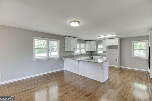 kitchen featuring light stone counters, white cabinetry, a sink, and a peninsula