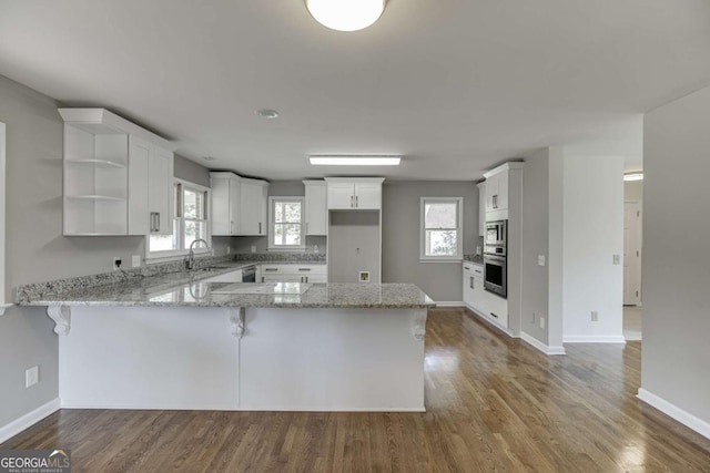 kitchen with wood finished floors, white cabinetry, a peninsula, and light stone countertops