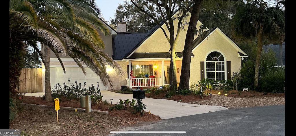 view of front of property with metal roof, a porch, concrete driveway, and stucco siding