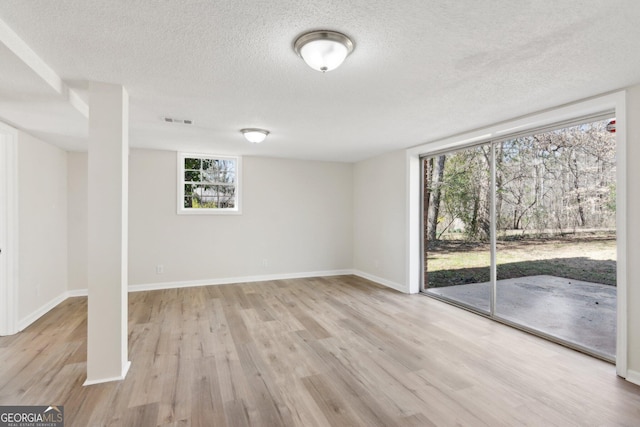 empty room with light wood-style flooring, a textured ceiling, visible vents, and baseboards