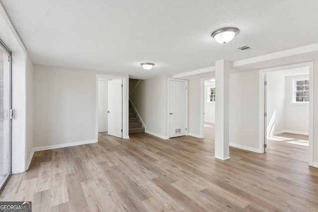 below grade area featuring light wood-style floors, visible vents, a textured ceiling, and stairs