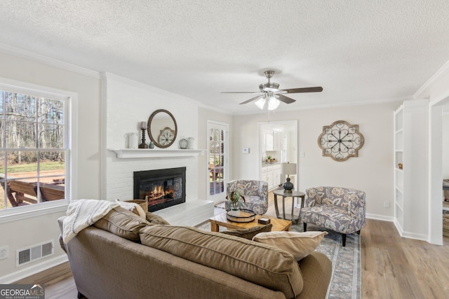 living room featuring crown molding, a fireplace, visible vents, a textured ceiling, and wood finished floors