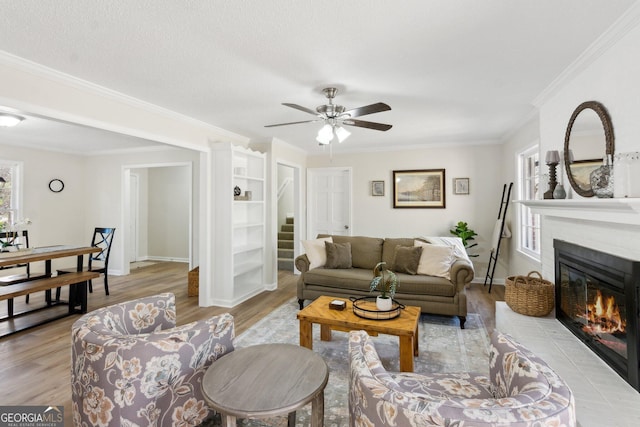 living area with ornamental molding, light wood finished floors, stairway, and a glass covered fireplace