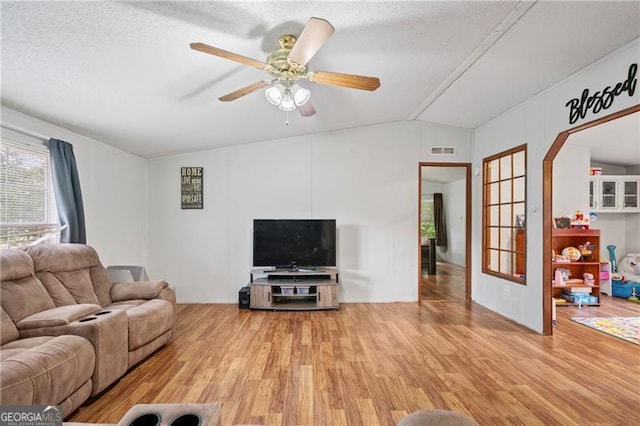 living area with arched walkways, lofted ceiling, visible vents, ceiling fan, and wood finished floors