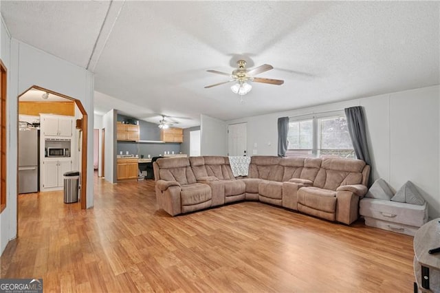 living area with light wood-style floors, ceiling fan, arched walkways, and a textured ceiling