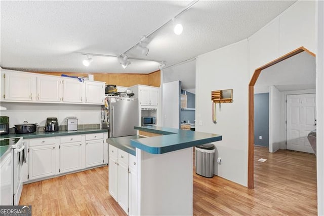 kitchen featuring a textured ceiling, stainless steel appliances, white cabinetry, light wood-type flooring, and dark countertops