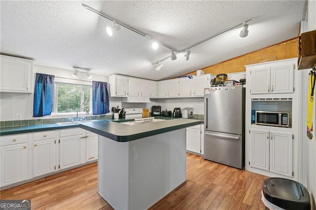 kitchen featuring stainless steel appliances, a sink, white cabinetry, vaulted ceiling, and light wood-type flooring