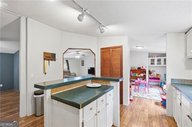 kitchen featuring a textured ceiling, ceiling fan, light wood-style flooring, white cabinets, and dark countertops