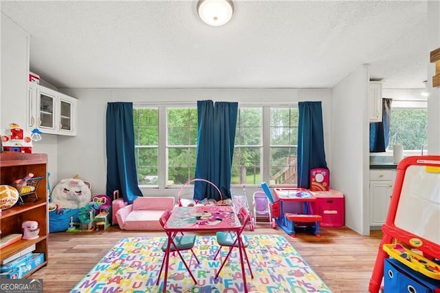 recreation room featuring light wood-style flooring and a textured ceiling