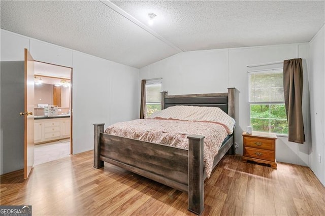 bedroom with vaulted ceiling, a textured ceiling, ensuite bathroom, and light wood-style floors