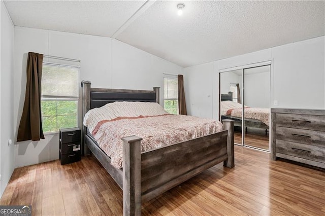 bedroom featuring a closet, vaulted ceiling, a textured ceiling, and wood finished floors