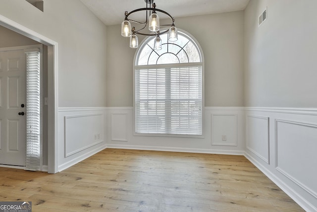 unfurnished dining area with a wainscoted wall, visible vents, a decorative wall, light wood-style flooring, and a chandelier