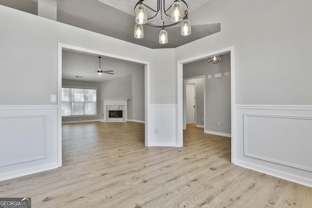 unfurnished living room with wainscoting, a premium fireplace, wood finished floors, and ceiling fan with notable chandelier