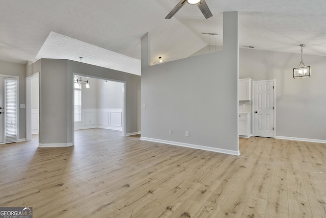 unfurnished living room featuring visible vents, baseboards, light wood-style flooring, high vaulted ceiling, and ceiling fan with notable chandelier