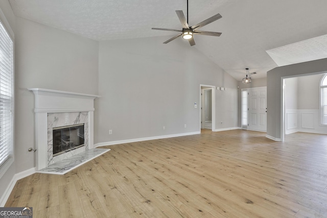 unfurnished living room with ceiling fan, a textured ceiling, lofted ceiling, a premium fireplace, and wood finished floors