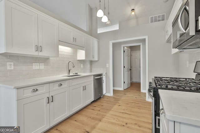 kitchen featuring visible vents, appliances with stainless steel finishes, a sink, white cabinetry, and backsplash