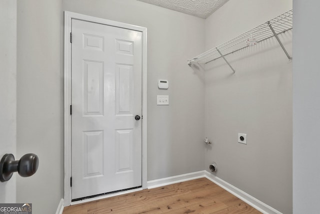 laundry room featuring a textured ceiling, laundry area, baseboards, light wood-type flooring, and electric dryer hookup