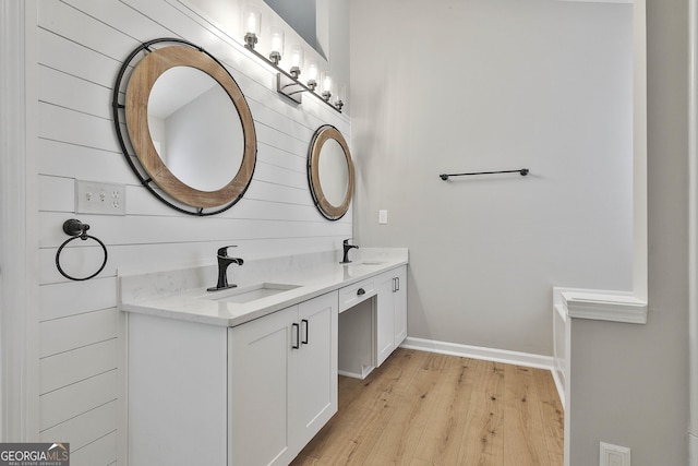 bathroom featuring double vanity, baseboards, a sink, and wood finished floors