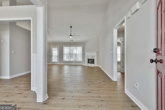 unfurnished living room featuring light wood-type flooring, baseboards, a ceiling fan, and a high end fireplace