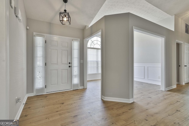 entrance foyer with a textured ceiling, visible vents, baseboards, vaulted ceiling, and light wood-type flooring