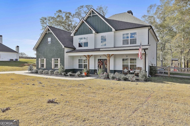 view of front of property with brick siding, a chimney, covered porch, board and batten siding, and a front lawn