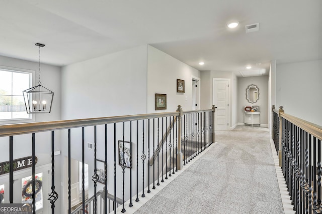 hall with carpet, visible vents, an inviting chandelier, attic access, and an upstairs landing