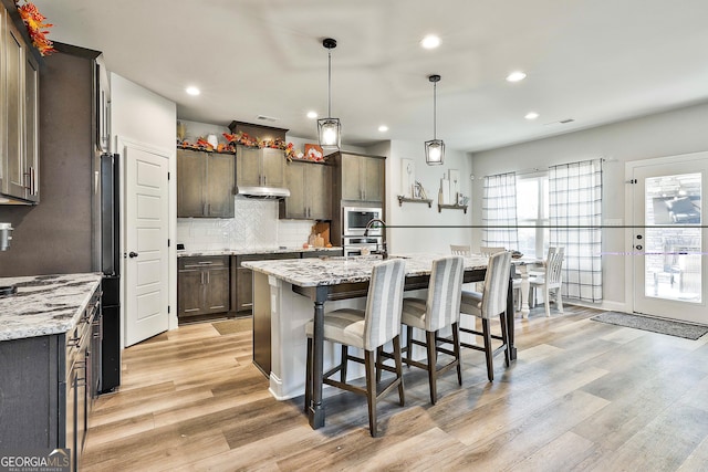 kitchen featuring light wood-type flooring, under cabinet range hood, stainless steel appliances, and decorative backsplash