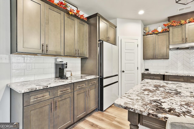 kitchen with light wood-type flooring, freestanding refrigerator, under cabinet range hood, and light stone counters