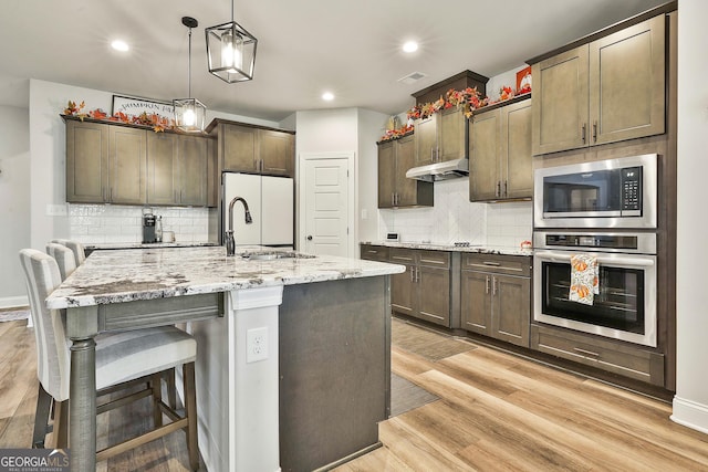 kitchen with light wood-style floors, freestanding refrigerator, built in microwave, oven, and under cabinet range hood