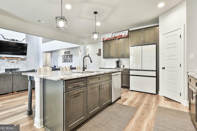 kitchen with light wood finished floors, dishwashing machine, open floor plan, freestanding refrigerator, and a sink