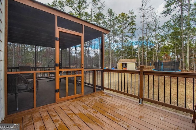 wooden deck featuring a trampoline, an outbuilding, a sunroom, and a storage shed