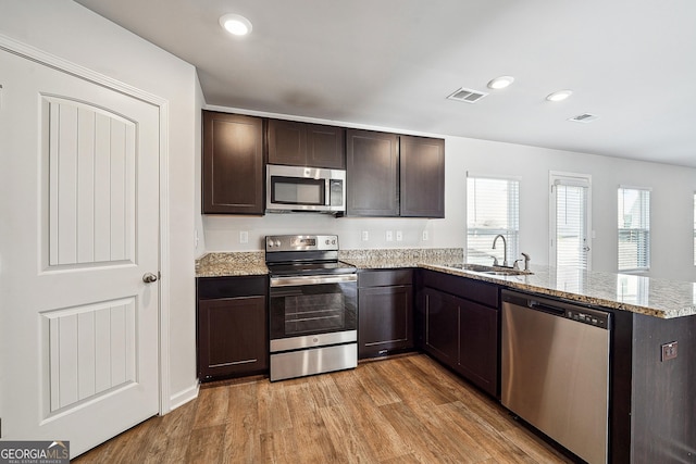 kitchen with visible vents, appliances with stainless steel finishes, dark brown cabinets, light wood-style floors, and a sink