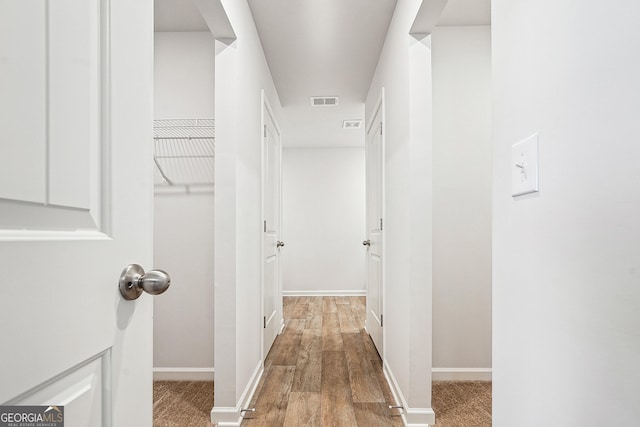 hall featuring visible vents, baseboards, and wood finished floors