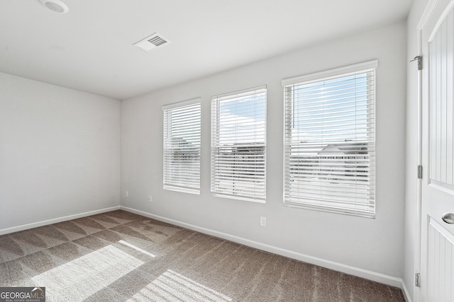 empty room with a wealth of natural light, baseboards, visible vents, and carpet flooring