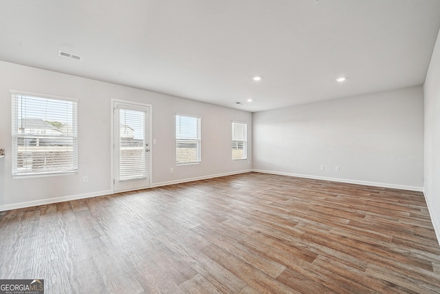 unfurnished living room featuring visible vents, plenty of natural light, baseboards, and wood finished floors